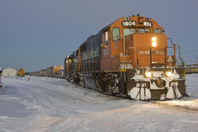 Walt Co Construction A freight train with the lead engine numbered 1804 is pulling several cars on a snow-covered track in a wintery scene near Smooth Rock Falls, Ontario. Another train can be seen in the distance. Smooth Rock Falls ON