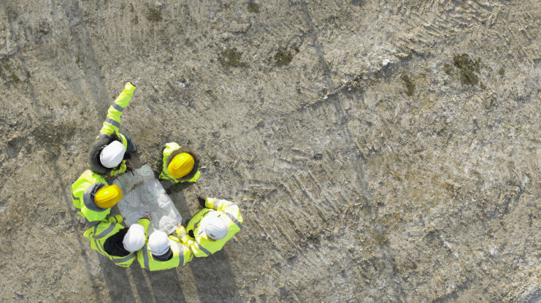 Walt Co Construction Aerial view of four construction workers in high-visibility clothing and hard hats looking at a blueprint on a Smooth Rock Falls Construction site in Smooth Rock Falls, Ontario. Smooth Rock Falls ON